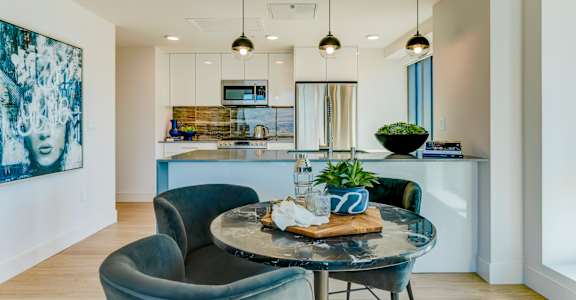 A modern dining room with a glass table and grey chairs.