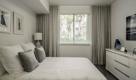 A bedroom with a large bed, a nightstand, and a window with curtains.