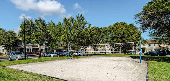 A volleyball court is surrounded by trees and parked cars.