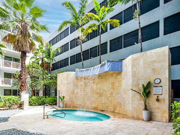 A pool surrounded by a stone wall and palm trees.