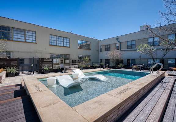 A pool with a wooden deck and a building in the background.