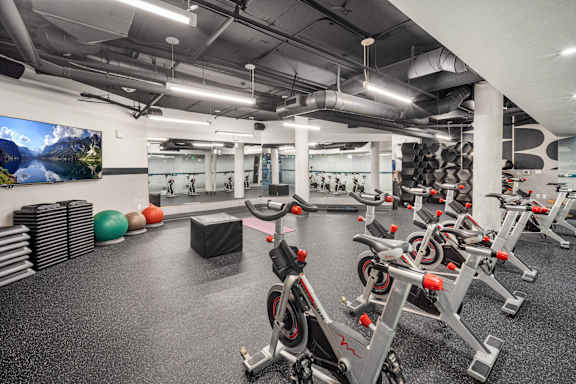 A gym with a row of stationary bikes and a TV mounted on the wall.