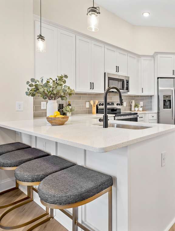 A kitchen with white cabinets and a white island with a vase of flowers on it.