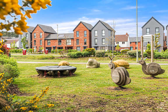 A park with sculptures of snails and a bench in front of apartment buildings.