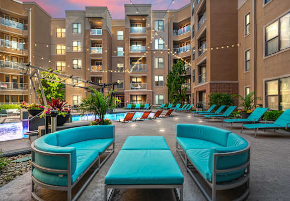 A large outdoor seating area with blue couches and a pool in the foreground.
