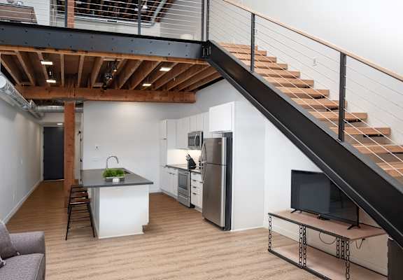 A living room with a staircase and a kitchen  at Bostad Apartments, Fargo, North Dakota, 58102