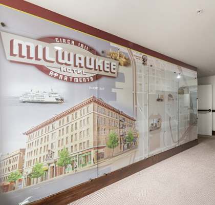 A wall mural in a room with a white ceiling and carpeted floor depicting a cityscape and a cruise ship.