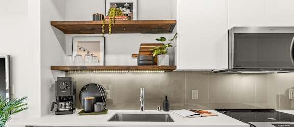 A modern kitchen with white cabinets and a wooden shelf above the sink.