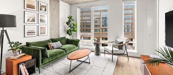 A living room with a green couch, a coffee table, and a large window with a view of a building.