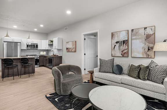A modern kitchen with a bar stool and a grey couch with pillows.