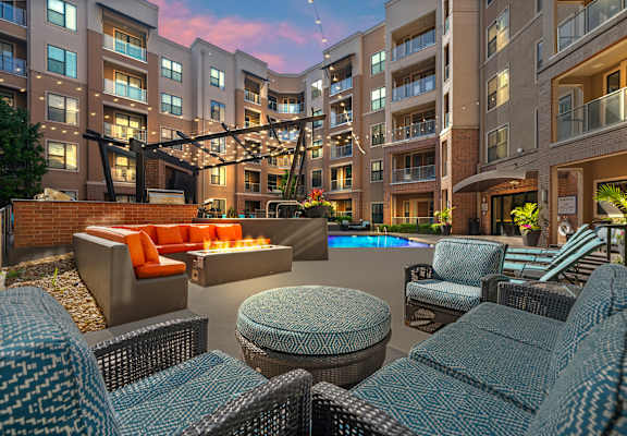A large outdoor seating area with wicker chairs and tables is surrounded by apartment buildings.