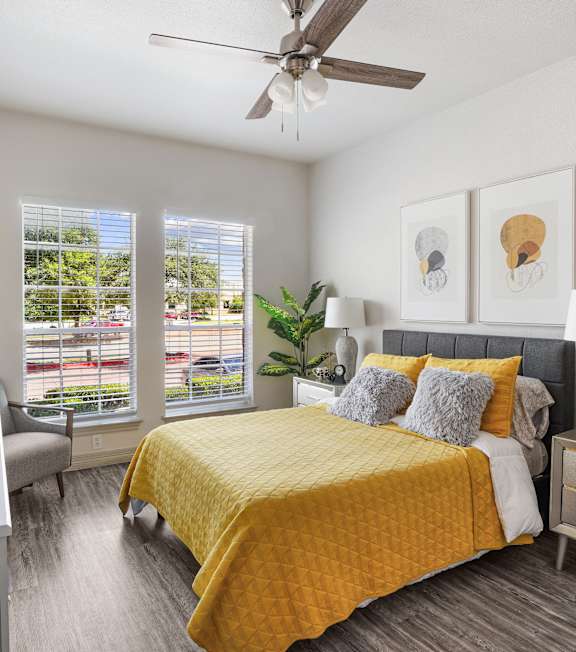 A bedroom with a yellow bedspread and a ceiling fan.