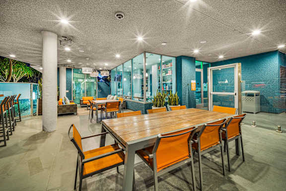 A long wooden table is surrounded by orange chairs in a room with a glass wall.