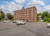 Thumbnail 7 of 7 - A parking lot with cars and a red brick building in the background.