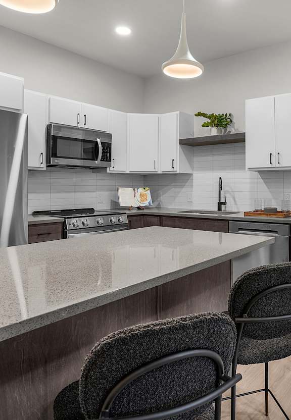 A kitchen with a refrigerator, microwave, and a counter with a chair.