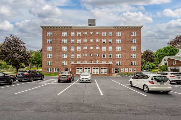 A parking lot in front of a red brick building with cars parked.