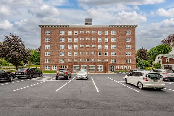 A parking lot in front of a red brick building with cars parked.