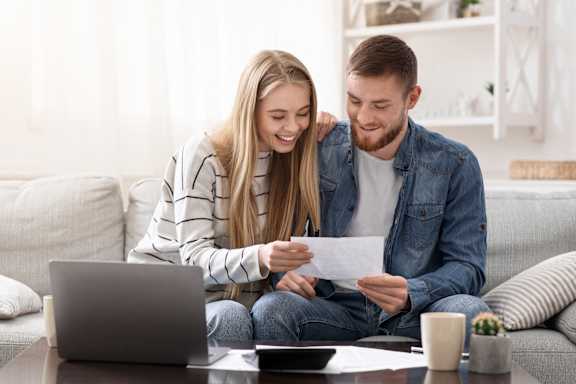 A man and a woman are sitting on a couch, looking at a piece of paper together.