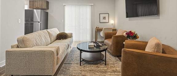 A living room with a beige couch, a coffee table, and a flat screen TV mounted on the wall.