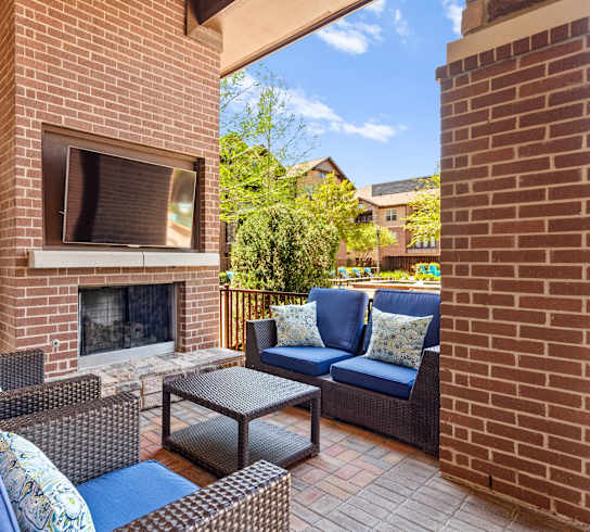 A patio with a brick fireplace and blue cushions.at Cypress at Lewisville Apartment Homes, Lewisville, TX 75067