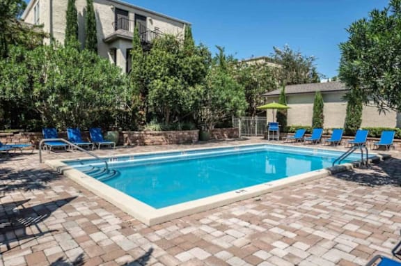 A small pool surrounded by a brick patio and blue lounge chairs.