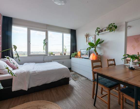A bedroom with a bed, a table, and a window overlooking the ocean.