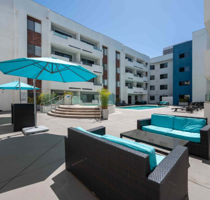 an outdoor lounge area with a turquoise umbrella in front of an apartment building