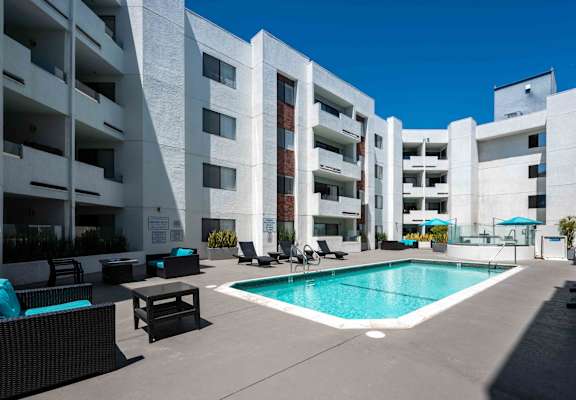 a swimming pool with chaise lounge chairs and umbrellas in front of a white building