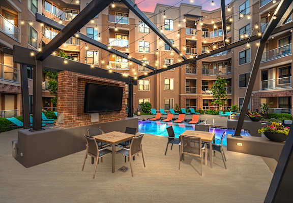 A modern outdoor patio area with a television, seating, and a pool.