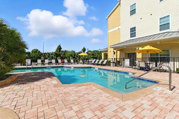 A large outdoor swimming pool surrounded by a brick patio and lounge chairs.