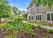 Thumbnail 46 of 54 - A building with a grey siding and white trim is surrounded by a garden with green plants.