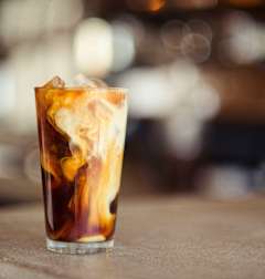 A glass of iced coffee with ice cubes on a table.