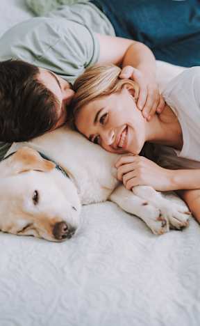 A couple is lying on a bed with their dog.