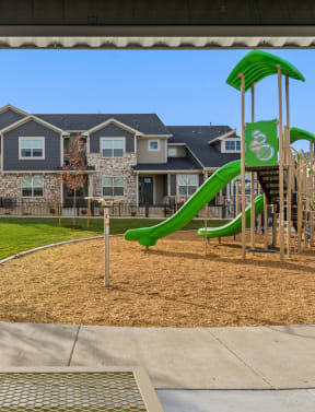 a playground with a green slide in front of an apartment building