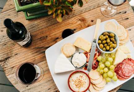 A wooden table with a plate of cheese, crackers, and grapes.