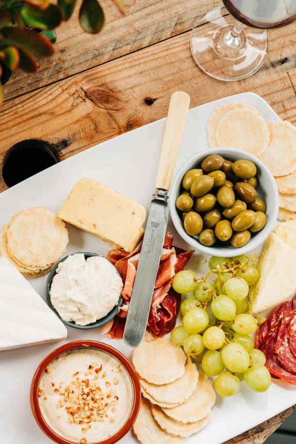 a plate of cheese and grapes on a table with a bottle of wine