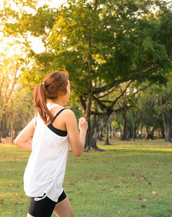 A woman in a white shirt and black shorts is running in a park.