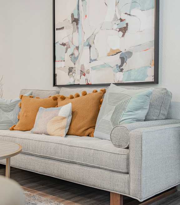 A living room with a grey couch, a round table, and a large abstract painting on the wall.