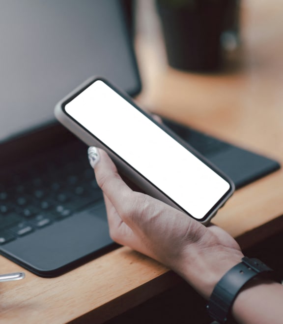 a person holding a cell phone in front of a laptop computer
