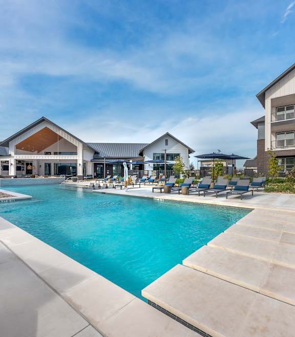 A large swimming pool is surrounded by a concrete patio and lounge chairs.