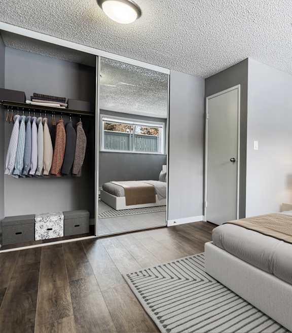 A bedroom with a large bed and a closet with clothes hanging.