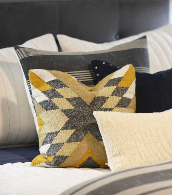 A bed with a striped comforter and a yellow and grey pillow.