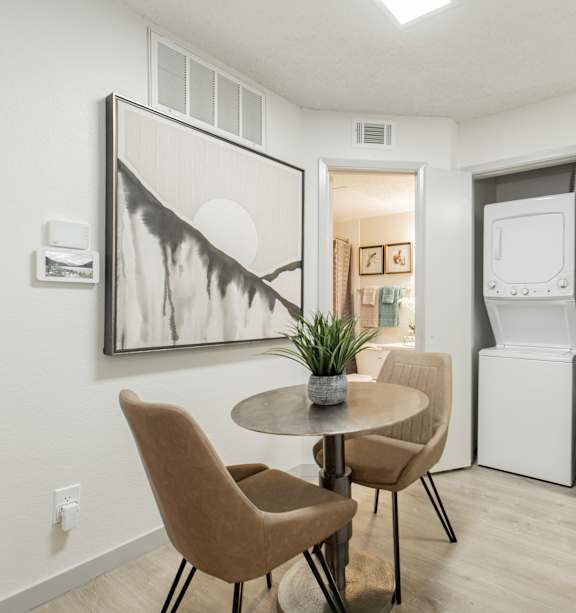 A dining room with a table and chairs and a framed artwork on the wall.
