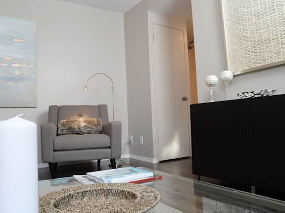 A grey chair with a pillow is in front of a lit fireplace.