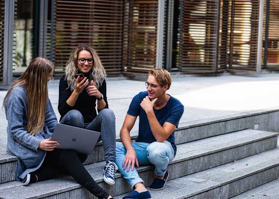 Three people sitting on steps with a laptop and a cell phone.
