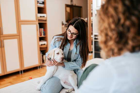 A woman in a blue robe is sitting on a bed with a dog.