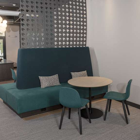 A blue couch with a white pillow is in the middle of a room with a round table and chairs.
