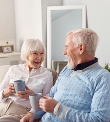An older couple sitting on a couch holding cups of coffee