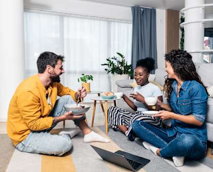 Three people are sitting on the floor eating food.