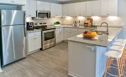 A kitchen with a refrigerator, microwave, oven, sink, and bar stools.